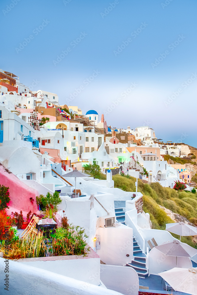 Picturesque Citiscape of Oia Village Houses and Classic Church with Bell Located on Volcanic Caldera Hills on Santorini Island During Sunset.