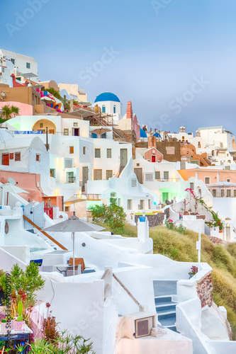 Cityscape of Oia Village on Santorini Island with Caldera Mountains On Background in Rays of Setting Sun.
