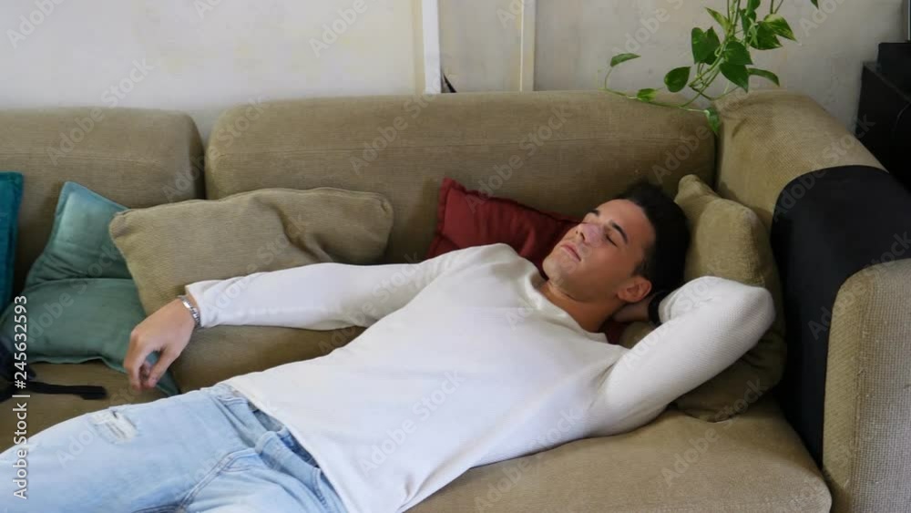 Young man arriving at home and falling on couch because he's very tired Young man arriving at home and falling on couch because he's very tired