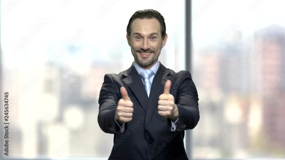 Attractive businessman giving two thumbs up. Middle-aged bearded CEO smiling and looking at camera. Blurred office window background. Attractive businessman giving two thumbs up. Middle-aged bearded CEO smiling and looking at camera. Blurred office window background.