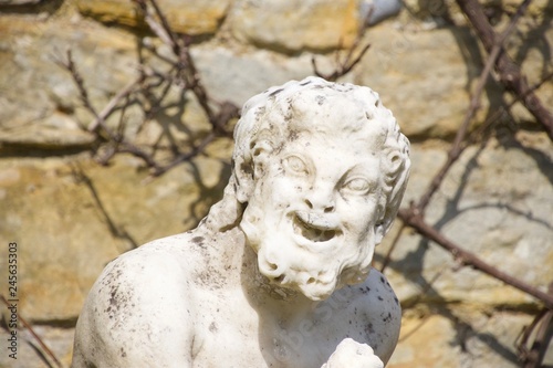 Φωτογραφία A stone statute, outdoors and in bright sunlight, of a funny old man with a shrivelled face and a big laughing grin that makes him look like a satyr or goblin