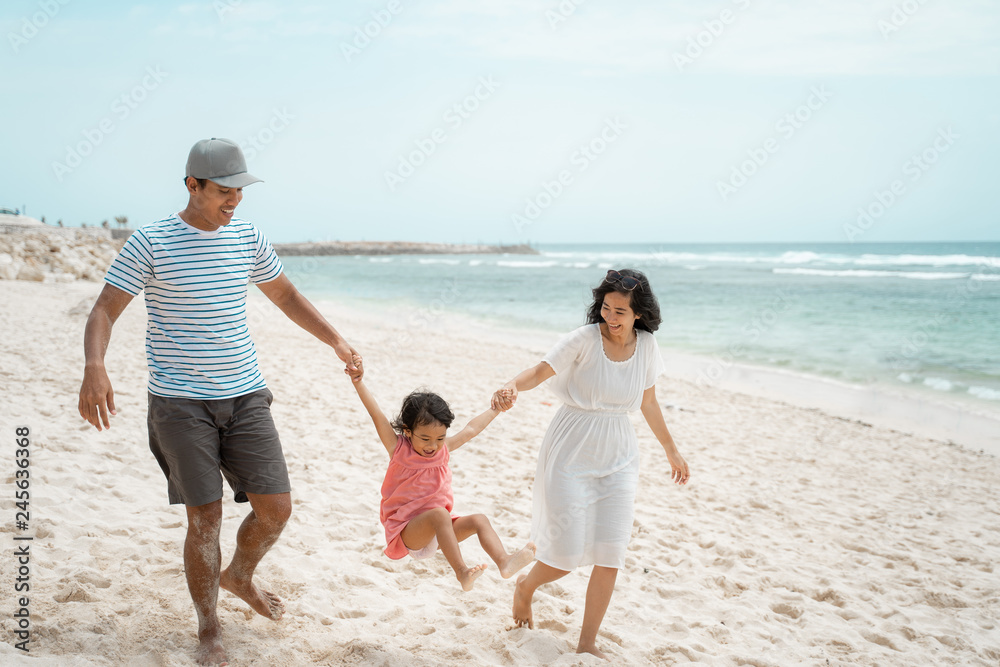 father and mother swinging a little girl on the beach