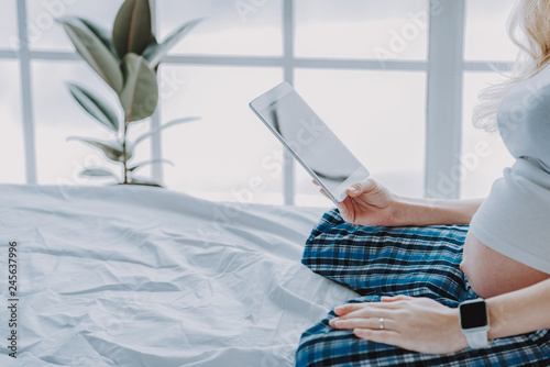 Expectant woman is reading in cozy bedroom
