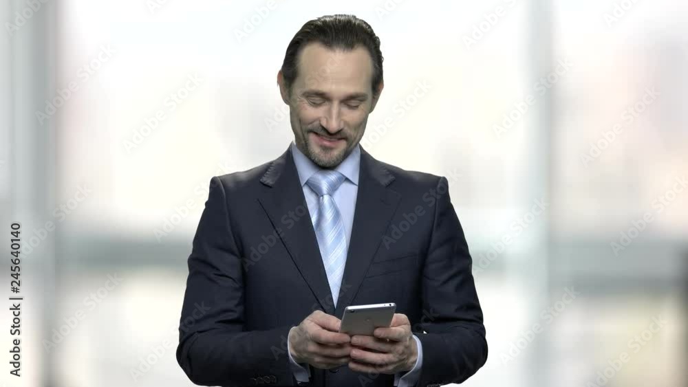 Surprised businessman looking at mobile phone. Smiling caucasian man in business suit typing a message on his smartphone. Surprised businessman looking at mobile phone. Smiling caucasian man in business suit typing a message on his smartphone.