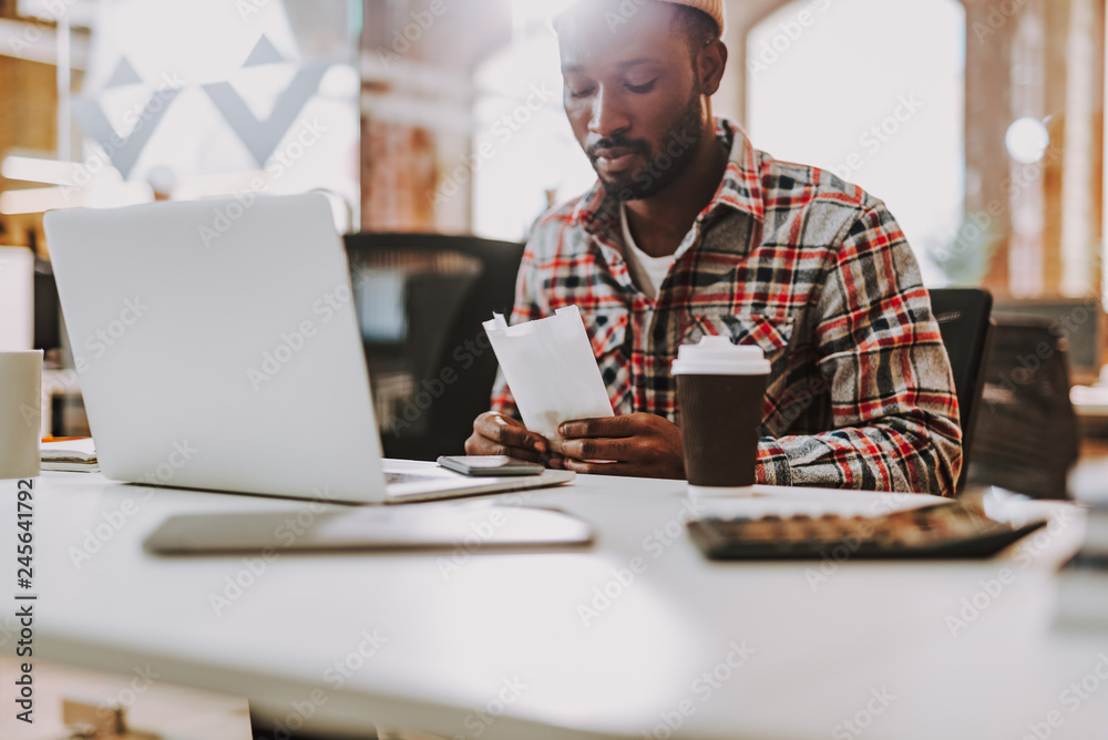 Calm Afro-American man looking at the paper bag in his hands