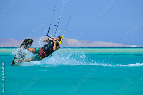 Kite surfing man surf sportsman with kite in sky on board in blue sea riding waves with water splash. Recreational activity, water sports, action, hobby and fun in summer time. Kiteboarding sport