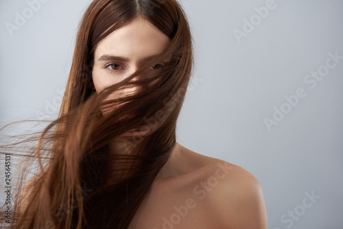 Young lady with hair strands on her face standing against light blue background