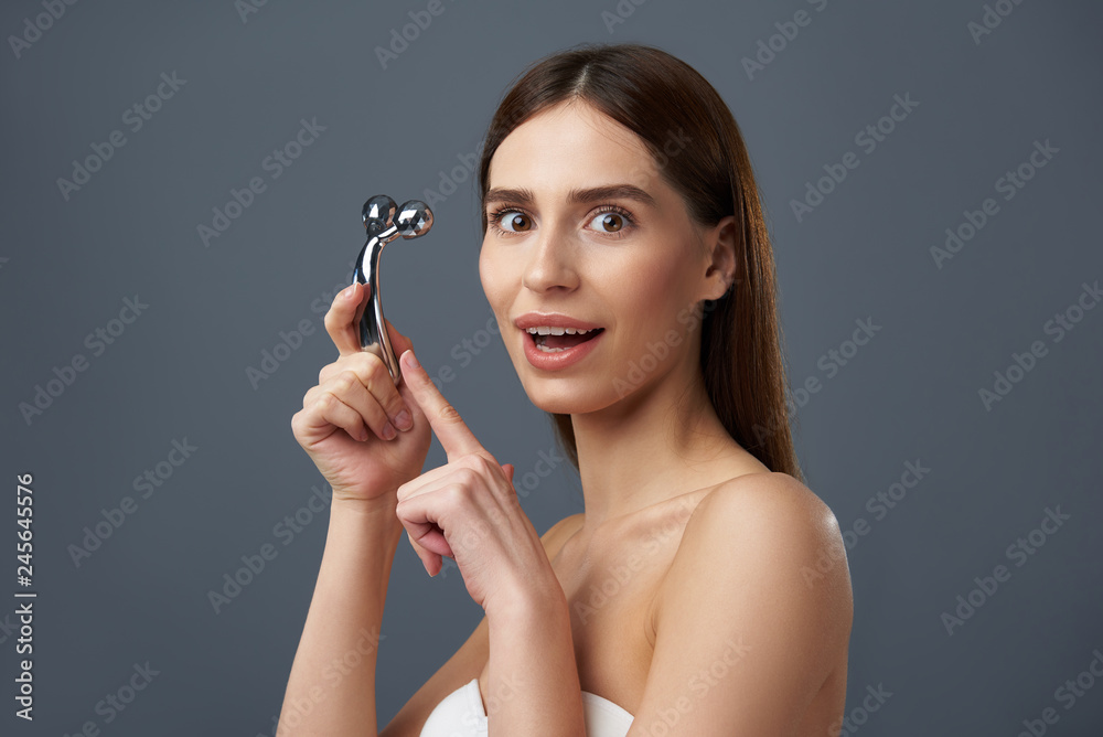 Excited young lady in white bra pointing at facial massager Excited young lady in white bra pointing at facial massager