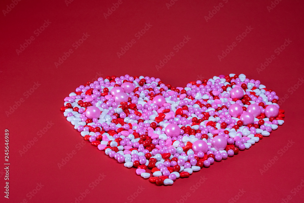 Large heart made of red white pink coated candy on a red background with text space. Valentine theme. Large heart made of red white pink coated candy on a red background with text space. Valentine theme.