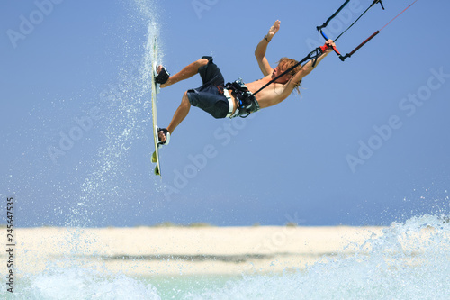 Professional kite boarding rider sportsman with kite in sky jumps high acrobatics kiteboarding trick with grab of kiteboard and huge water splash. Recreational activity, extreme active air sports