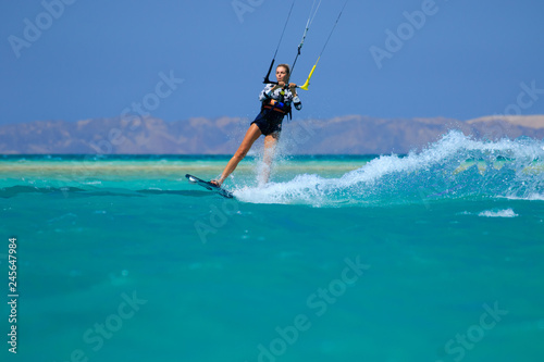 Kite surfing girl in sexy swimsuit with kite in sky on board in blue sea riding waves with water splash. Recreational activity  water sports  action  hobby and fun in summer time. Kiteboarding sport