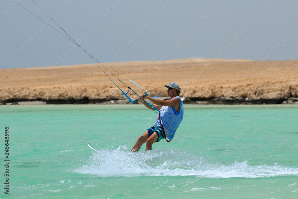 Kite surfing man surf sportsman with kite in sky on board in blue sea riding waves with water splash. Recreational activity, water sports, action, hobby and fun in summer time. Kiteboarding sport Kite surfing man surf sportsman with kite in sky on board in blue sea riding waves with water splash. Recreational activity, water sports, action, hobby and fun in summer time. Kiteboarding sport
