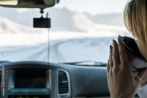 The girl in the passenger seat of the car drinking hot tea from a mug of a thermos, looking on the mountain winter road outside the car window © Евгений Медведев
