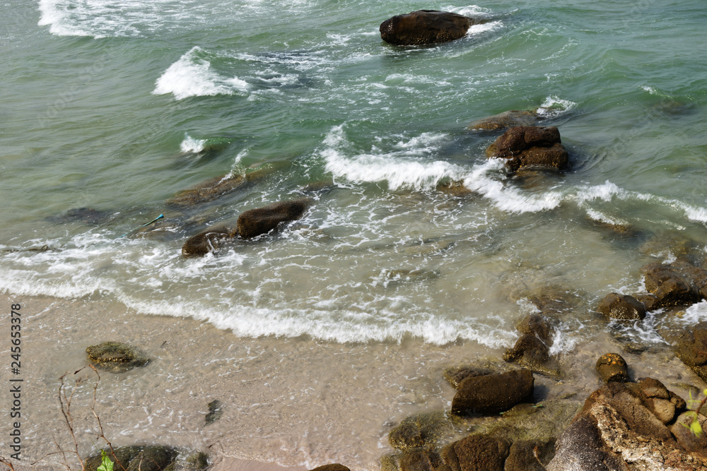 Fototapeta premium Green sea with wave splashing black rock and brown sand on the beach, Hua Hin , Thailand