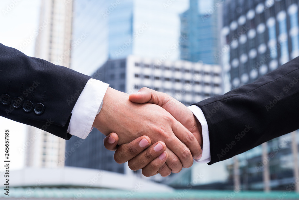 Two businessman dealing partners with shaking hands on urban city background.
