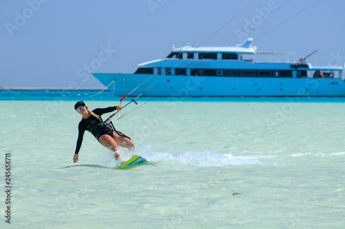 Kite surfing girl in sexy swimsuit with kite in sky on board in blue sea riding waves with water splash. Recreational activity, water sports, action, hobby and fun in summer time. Kiteboarding sport