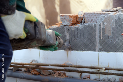 Fototapeta Naklejka Na Ścianę i Meble -  Man professional builder in dusty uniform breaks brick, concrete walls and tile with perforator. Concept overhaul, renovation, redevelopment of the walls of the office, kitchen in restaurant