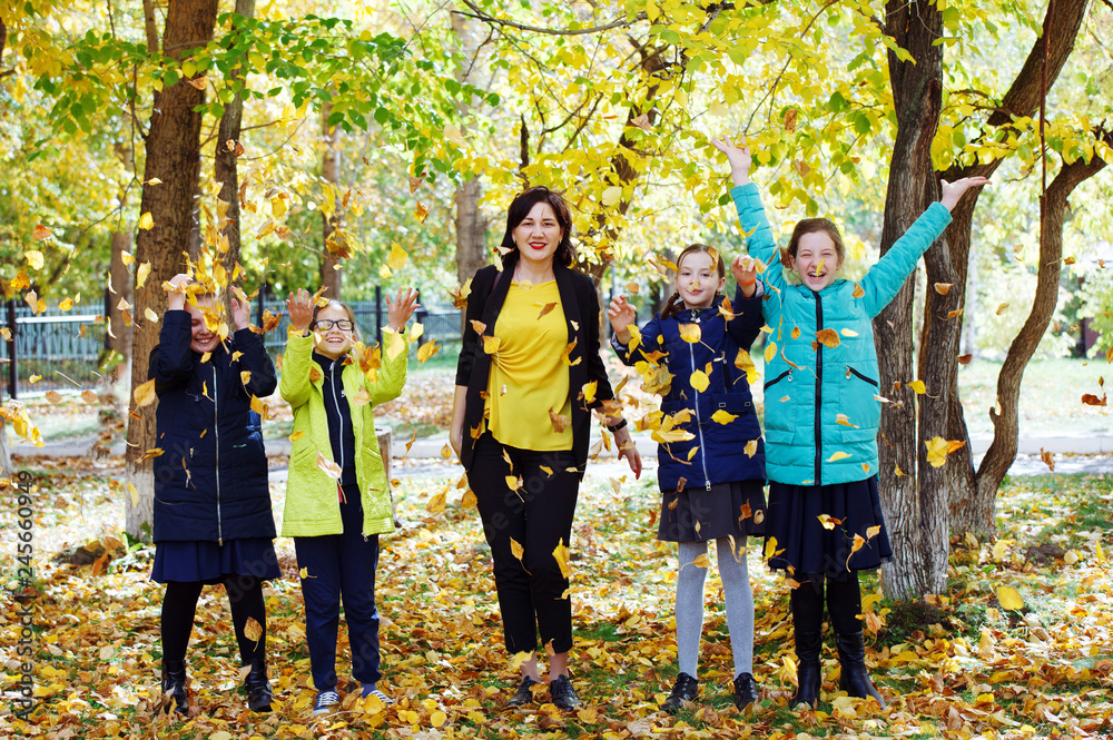 Young pretty girls teenagers in the autumn courtyard walk throw yellow leaves and rejoice.