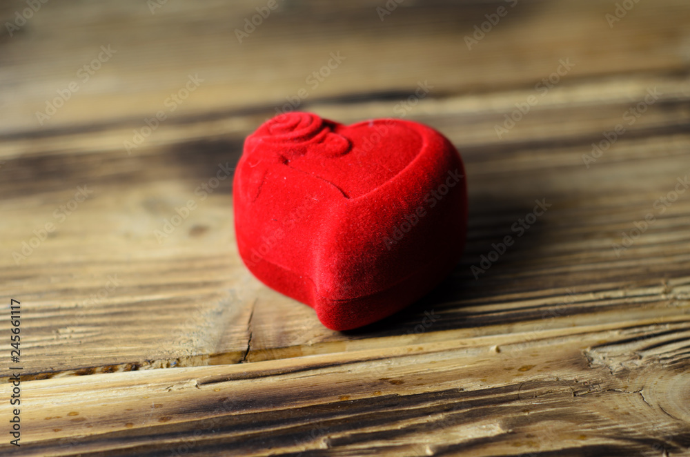 Red heart-shaped jewelry box on a wooden table Red heart-shaped jewelry box on a wooden table