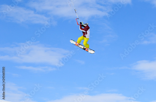 Professional kite boarding rider sportsman with kite in sky jumps high acrobatics kite boarding trick with grab of kite board. Recreational activity, extreme active sports, snow kiting ski snowboard
