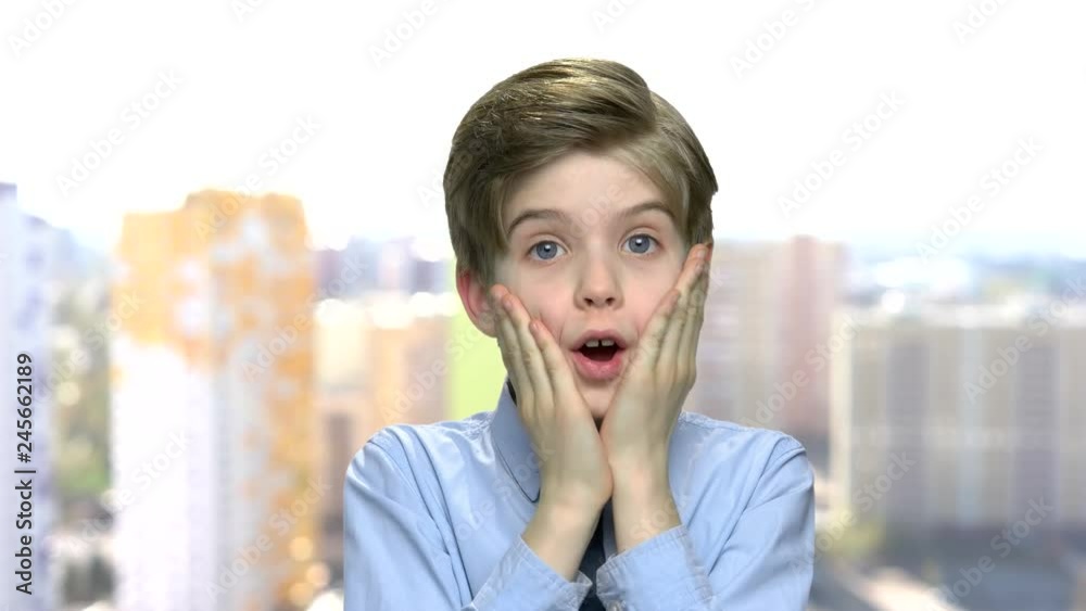 Scared preteen boy is screaming. Shocked frightened child boy holding hands on face. Blurred city buildings background. Scared preteen boy is screaming. Shocked frightened child boy holding hands on face. Blurred city buildings background.