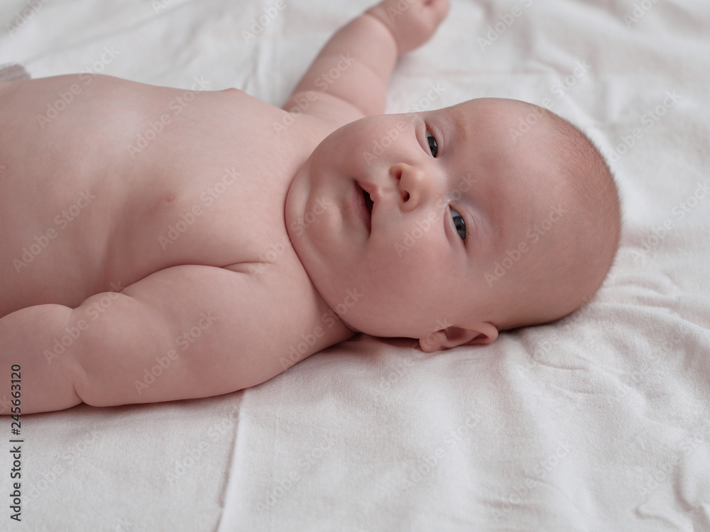 Baby with a concerned facial expression. The baby lies on a white linen cloth. Baby with a concerned facial expression. The baby lies on a white linen cloth.