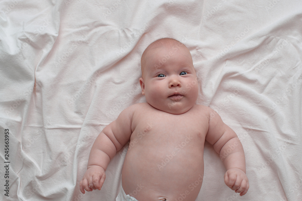 Happy and surprised blue-eyed baby. The baby lies on a white linen cloth. Happy and surprised blue-eyed baby. The baby lies on a white linen cloth.