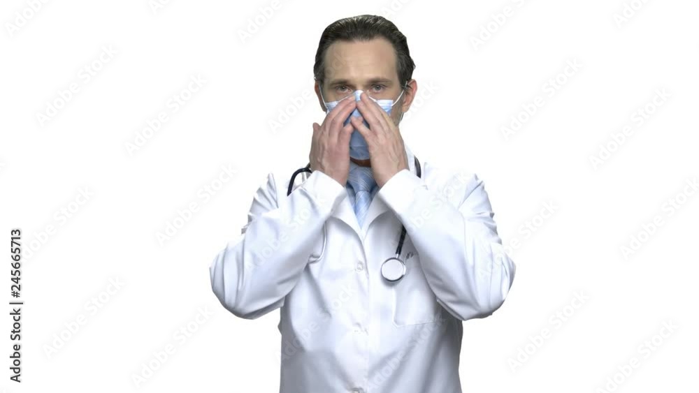Mature doctor with stethoscope puts on protective mask. Male physician in white coat puts on rubber gloves. Ready for examination. Isolated on white background. Mature doctor with stethoscope puts on protective mask. Male physician in white coat puts on rubber gloves. Ready for examination. Isolated on white background.