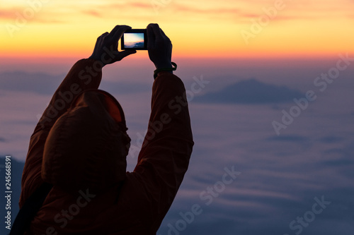 silhouette of person in orange jacket take a photo of sunrise and fog © amstockphoto