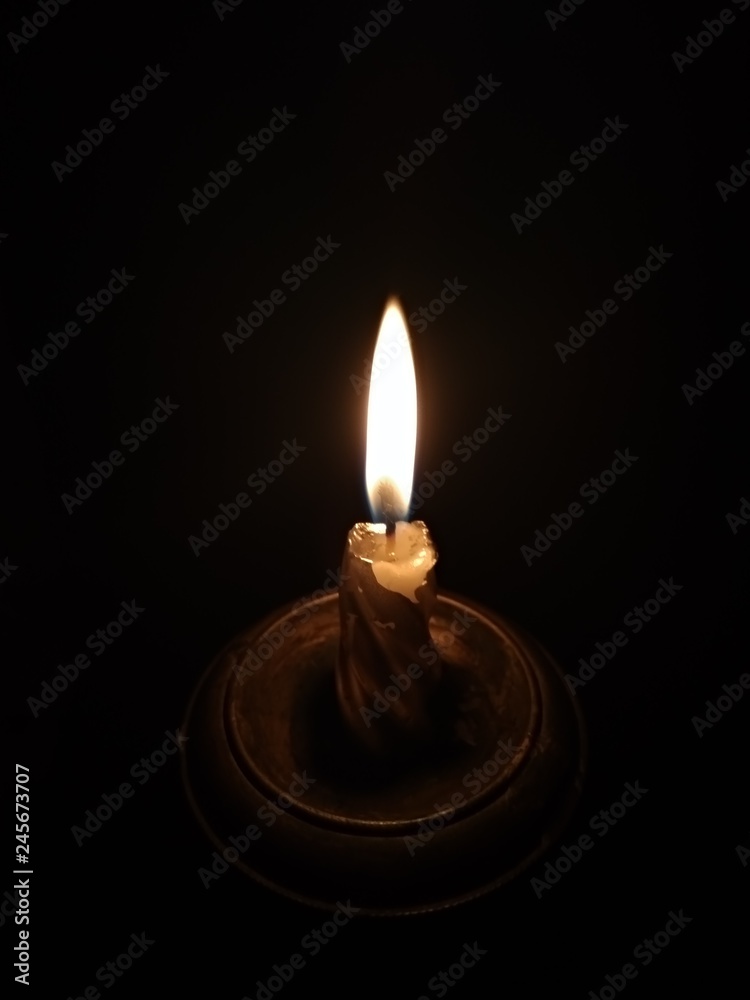 Burning candle in a candlestick on a black background Burning candle in a candlestick on a black background