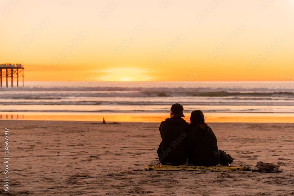 Young couple sitting on the beach watching golden sunset.