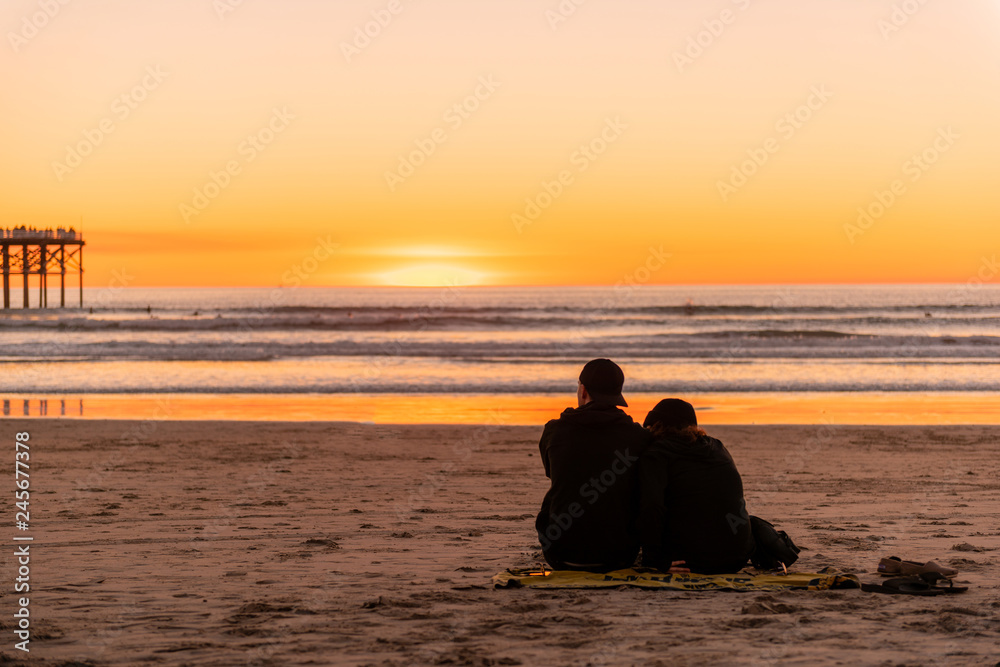 Young couple sitting on the beach watching golden sunset.