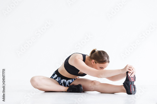 Beautiful young athletic girl doing exercises for stretching the ligaments and muscles of the legs before training sitting on the floor in the gym