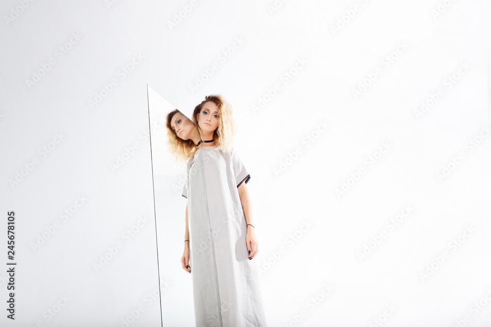 Art fashion studio portrait of elegant blonde woman and her reflection in the mirror on white background. An illusion, beautiful girl surreal image. digital narcissism concept minimal flat design Art fashion studio portrait of elegant blonde woman and her reflection in the mirror on white background. An illusion, beautiful girl surreal image. digital narcissism concept minimal flat design