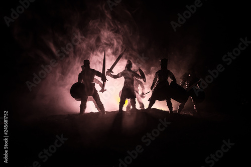 Medieval battle scene. Silhouettes of figures as separate objects, fight between warriors on dark toned foggy background. Night scene.