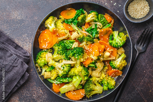 Vegan wok stir fry with broccoli and carrot in black dish.