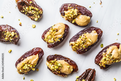 Dates stuffed with peanut butter and pistachios on white background.