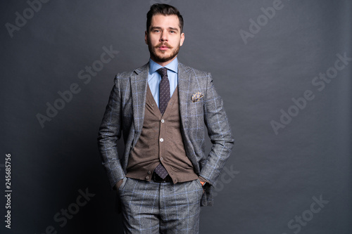 A confident elegant handsome young man standing in front of a grey background in a studio wearing a nice suit.