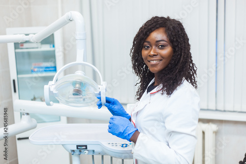 Fototapeta Naklejka Na Ścianę i Meble -  Portrait of female black dentist in dental office. She standing at her office and she has beautiful smile.
