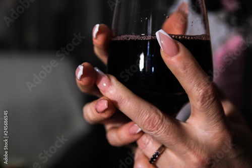 Woman's hands holding glass of wine. Nail art on hers nails.