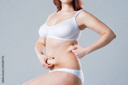 Woman with fat abdomen, overweight female body on gray background