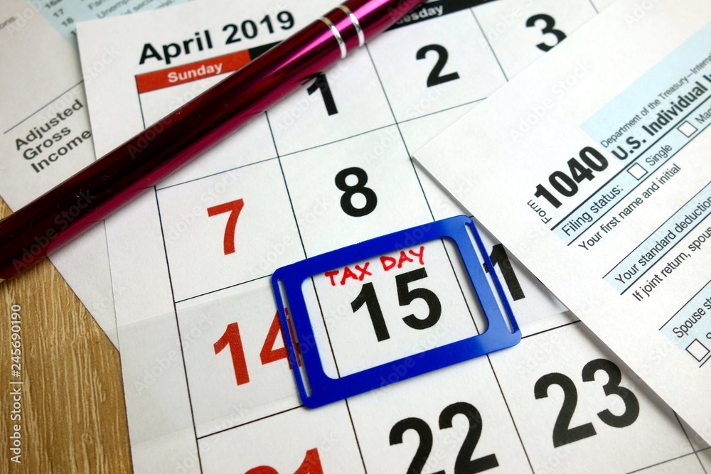 Monthly calendar showing date April 15th 2019 marked as tax day with 1040 form and pen Monthly calendar showing date April 15th 2019 marked as tax day with 1040 form and pen