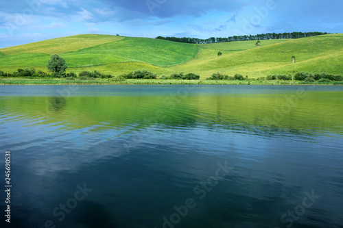 Beautiful natural background. Green hill, blue sky and blue water of the lake in Altai in Russia