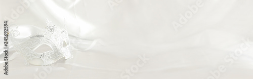 Banner of elegant and delicate white lace venetian mask over silk background.