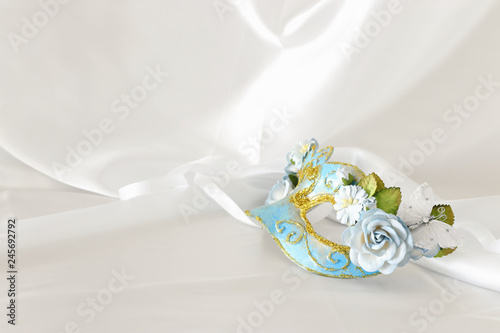Photo of elegant and delicate light blue venetian mask over white silk background.