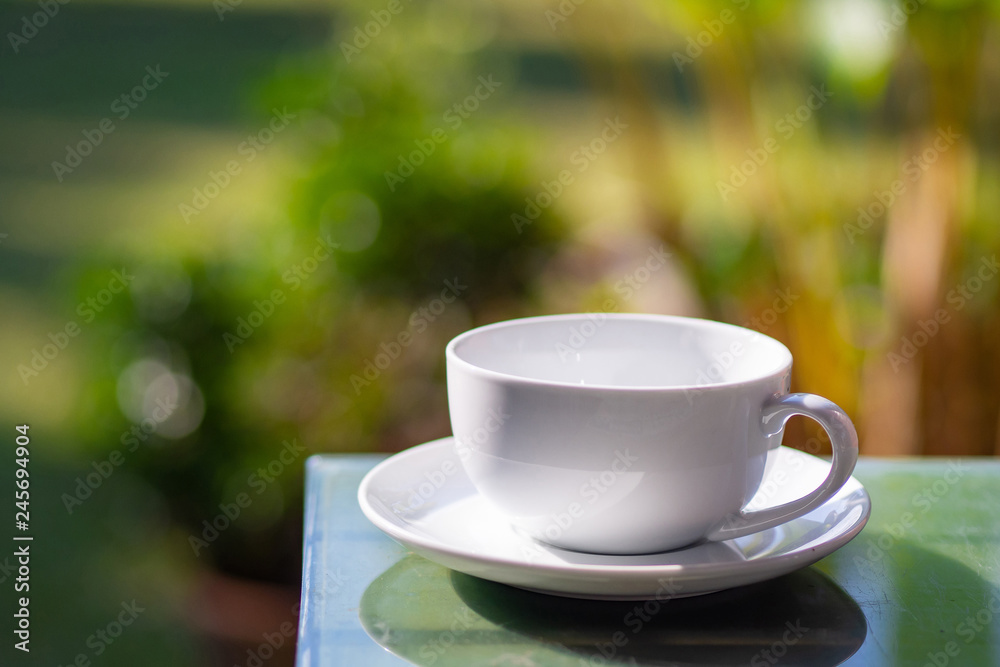 A white cup of coffee on table with natural background in the garden. A white cup of coffee on table with natural background in the garden.