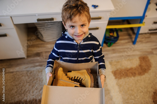 close up of a boy holding a open cardboard box with a pair of yellow leatrher boots