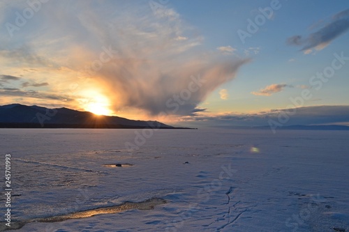 Sunset on the shore of a winter lake surrounded by hills