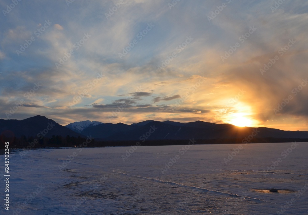 Sunset on the shore of a winter lake surrounded by hills
