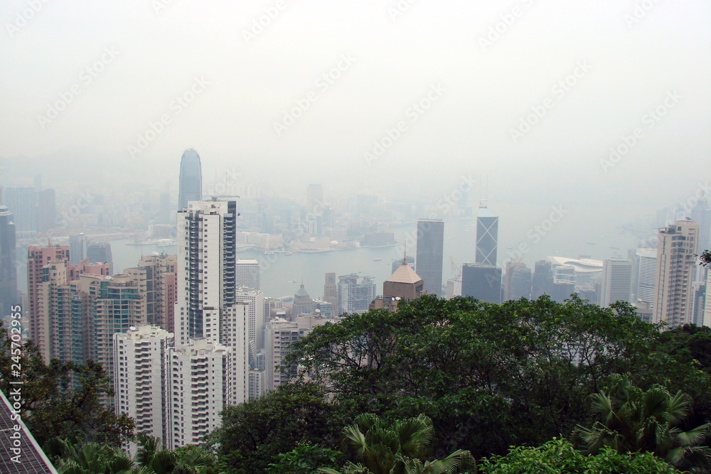 View of the mountain forest on the skyscrapers of the Asian megapolis, which are tightly surrounded by the coast of the Gulf, against the background of the cloudy spring sky.